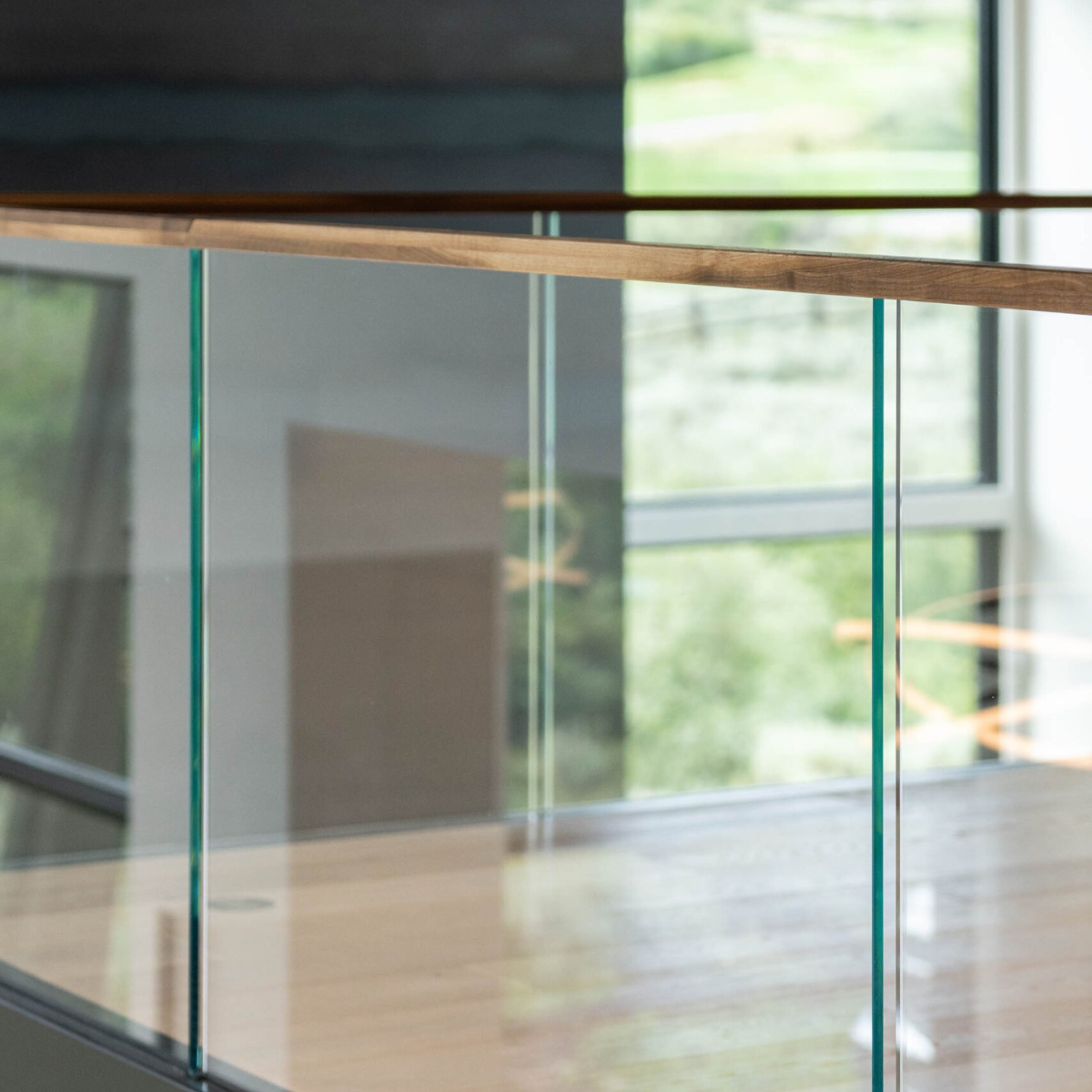 A corner of a balcony showing a clear glass railing with wood handrail