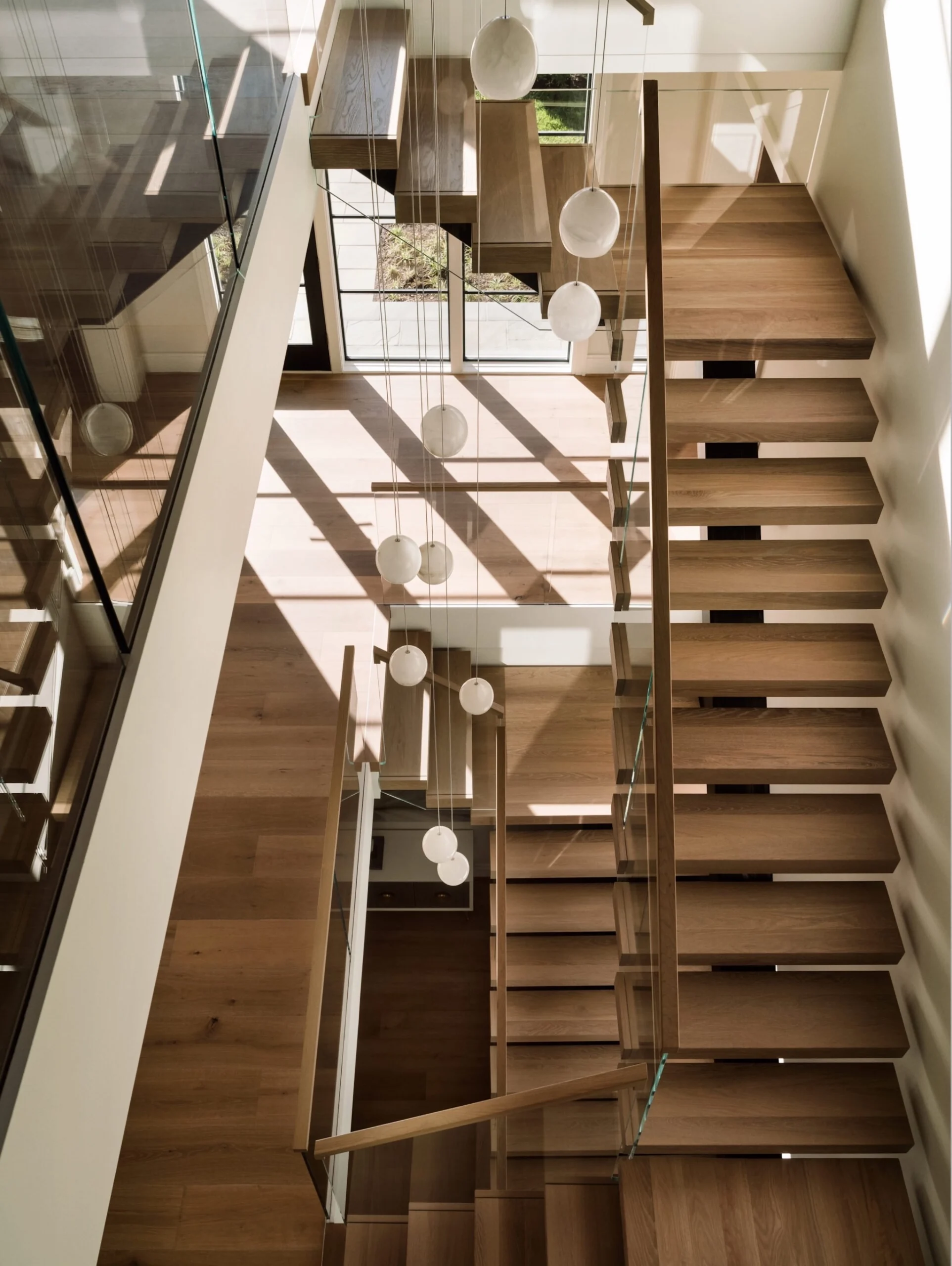 A top-down shot of a FLIGHT Mono staircase with a multiple-hanging-light chandelier descending through the U-shaped, two-floor layout.