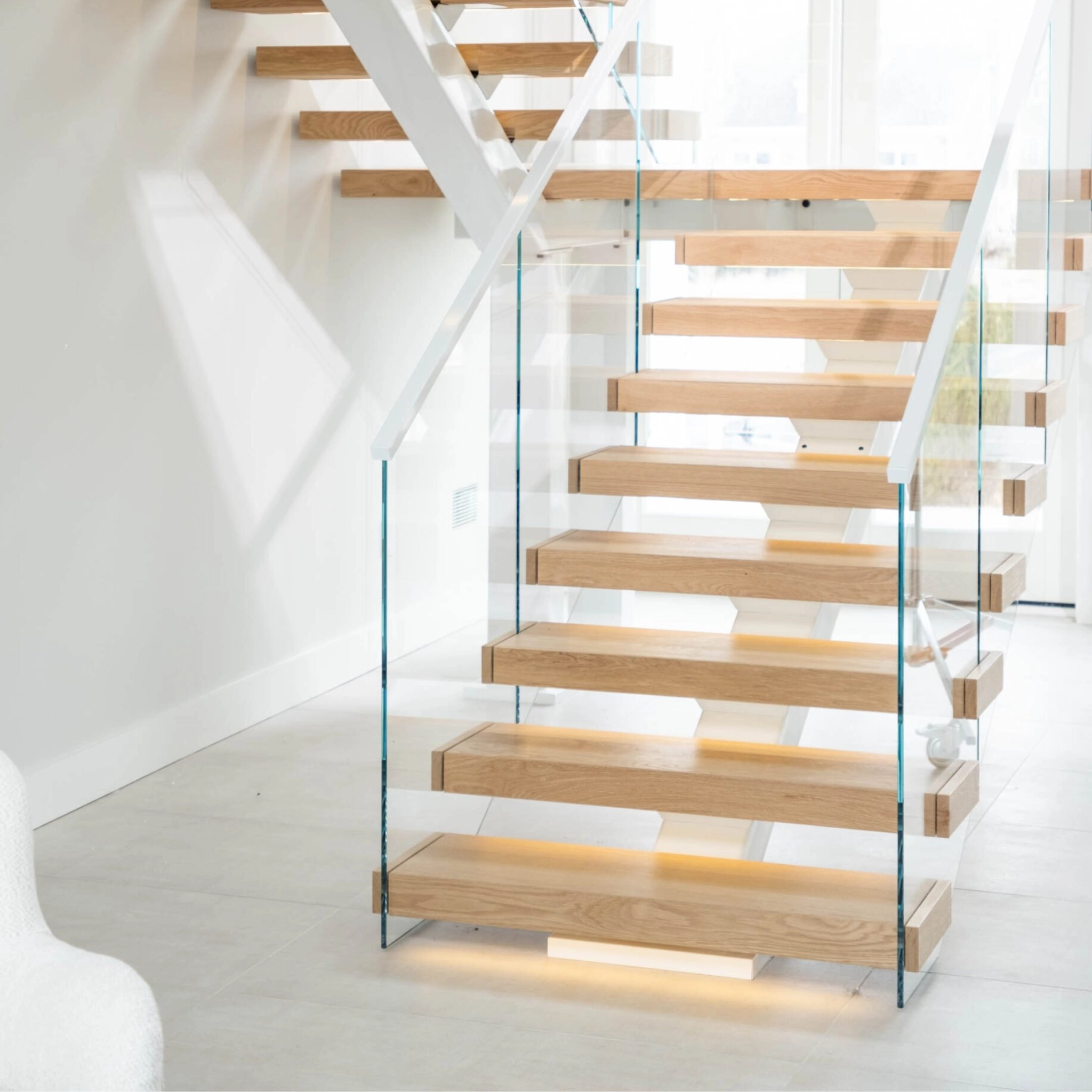 A FLIGHT Mono staircase with white powder-coated stringer and cap rail of Vedera glass railing, in a light-filled room.